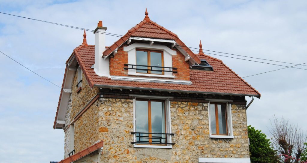 Maison original avec toiture en pente en tuiles mécanique rouge avec barrière noir métallique